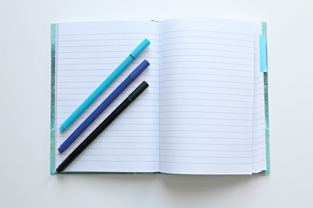 Estudar muito! 1 Foto de um caderno aberto com folhas em branco, e em cima dele três lápis em diagonal: o de cima azul-claro, o do meio azul-marinho e o de baixo preto, representando o propósito de estudar e aprender coisas novas. Fim da descrição.