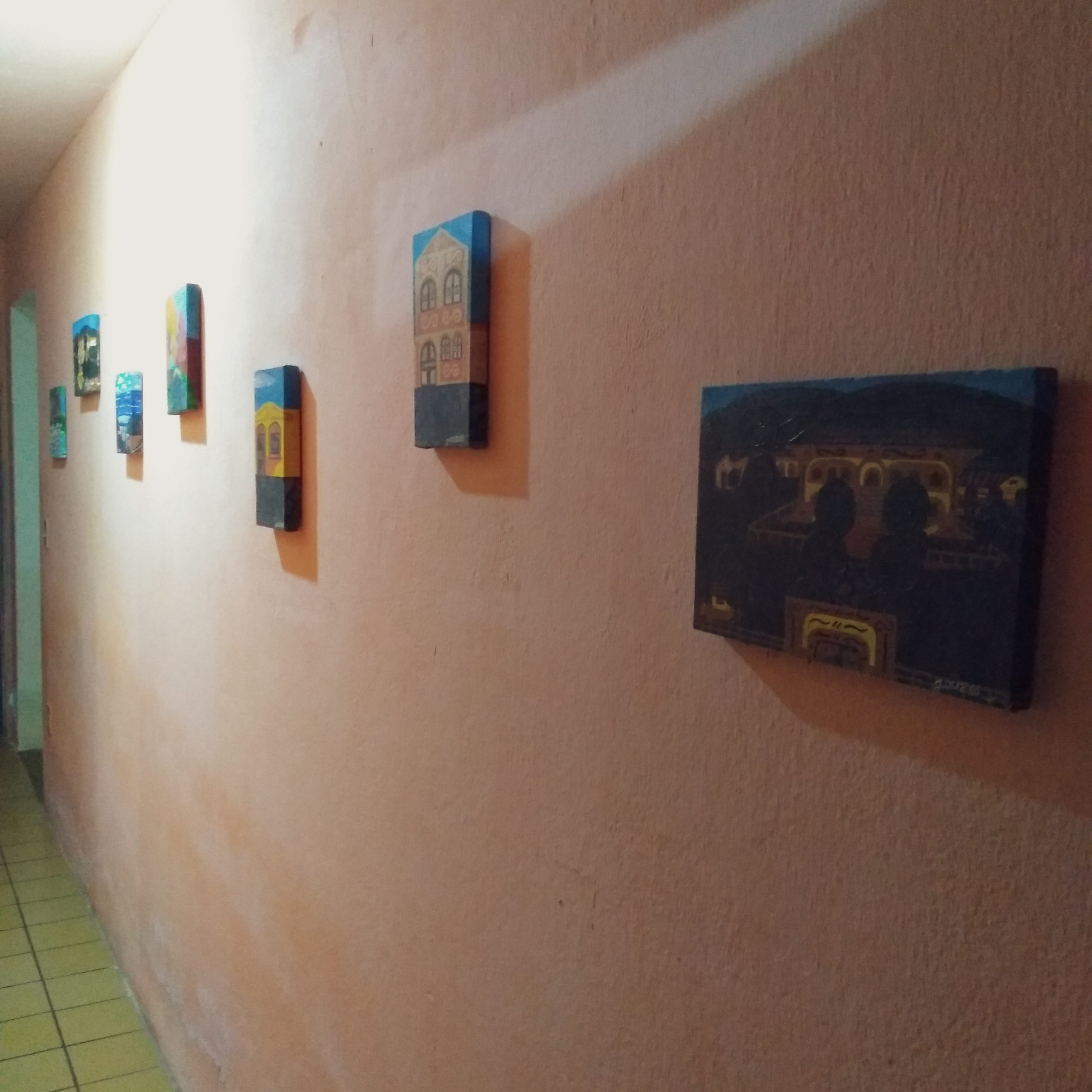 Foto da parede do corredor de casa, exibindo sete quadros pendurados nela. Fim da descrição.